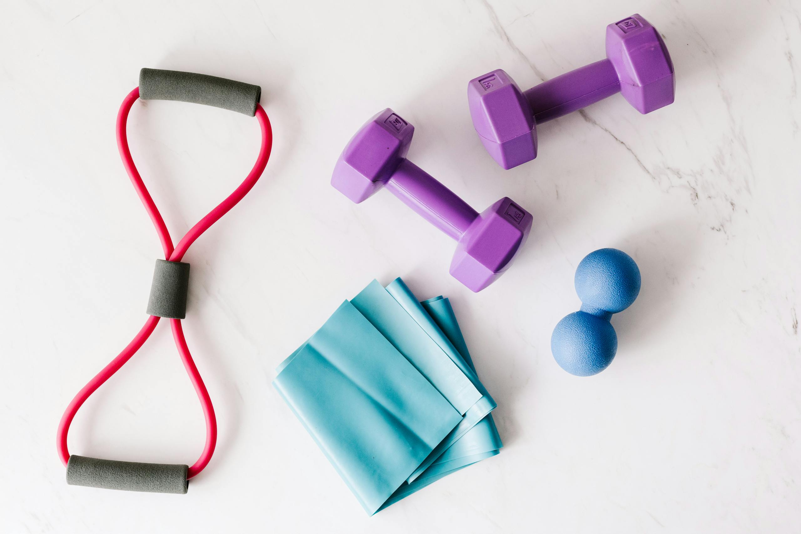 Colorful home workout equipment, including dumbbells and resistance bands, on a marble surface.