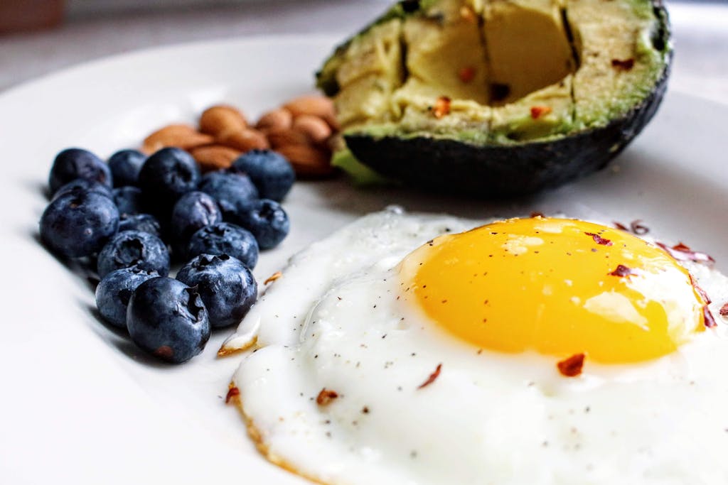 A nutritious breakfast featuring a fried egg, avocado, blueberries, and almonds.